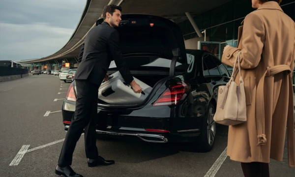 chauffeur putting client's luggage in the trunk of a black